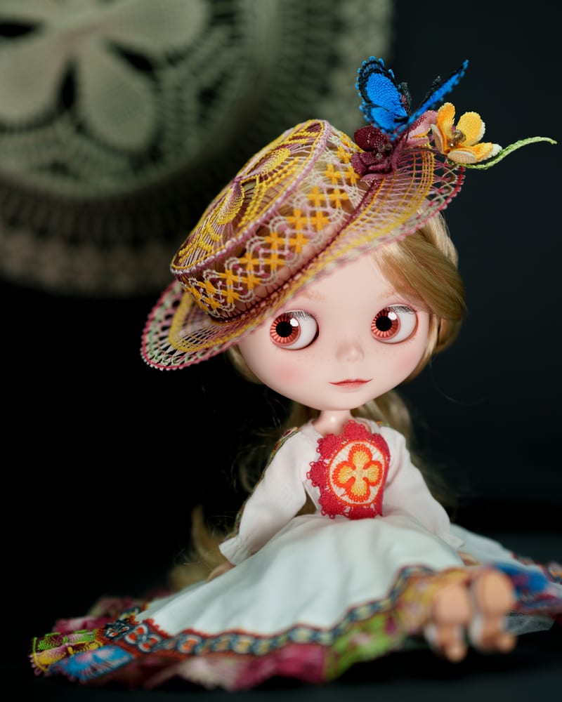 The doll seated against black, a Ñandutí doily hanging behind.