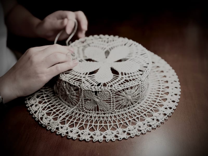 A hand drawing thread through the hat as it rests on the table, the brim still flat.