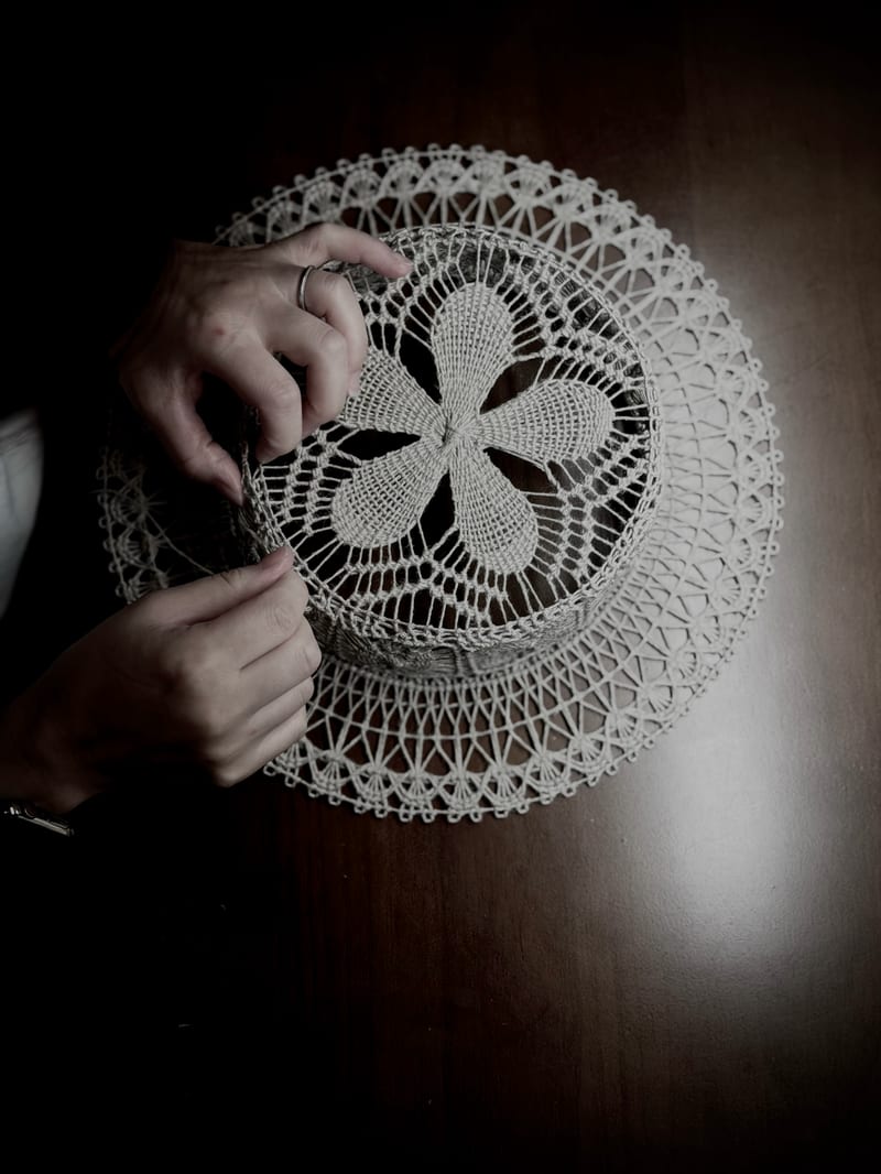 Two hands working the hat on a wooden table, its crown worked outward from the centre.